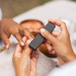 Close up of african hands of a qualified manicurist filing the nails of a young woman. Hands during manicure care session. Detail of a girl in a nail salon receiving manicure.